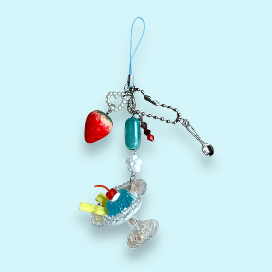 Handmade phone charm with jelly dessert dish, red strawberry charm, beads, and silver spoon on blue background