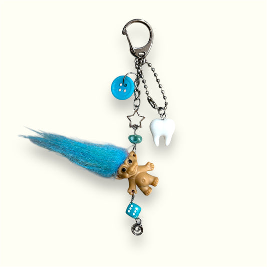 Handmade keychain with vintage troll doll, blue hair, tooth charm, dice bead, and star accents on cream background