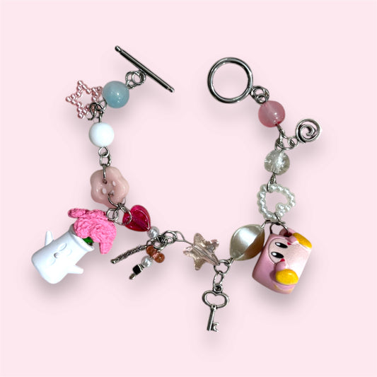 Handmade bracelet with Kirby block charm, pink flower vase, heart and star beads, and toggle clasp on pink background.