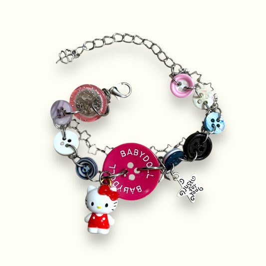 Colorful button bracelet with Hello Kitty charm and pink “Babydoll” centerpiece, displayed on a cream background.